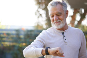 Senior Man Checking Health Monitor On Smart Watch In Garden At Home